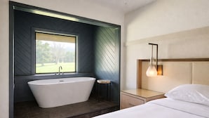 A modern bathroom with a freestanding bathtub, a window, and a bedside table with a lamp. - The Parkman - Great Smoky Mountains (Townsend)