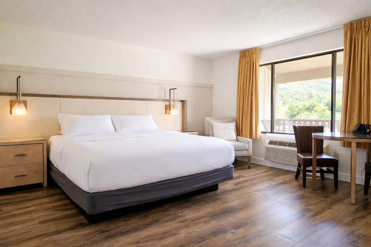 A hotel room with a large bed, bedside tables, a desk with a chair, and a window with curtains.
