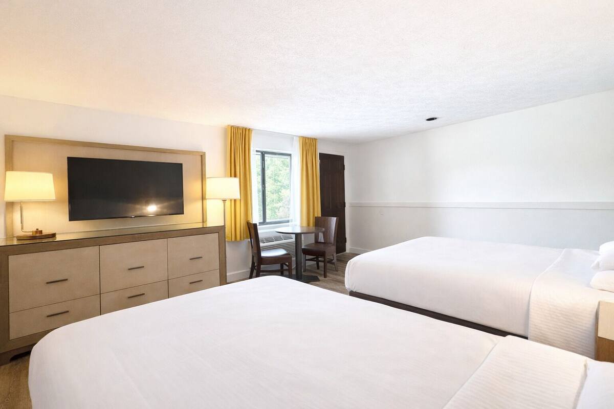 A hotel room with two beds, a desk with a chair, a TV, and a window with curtains.