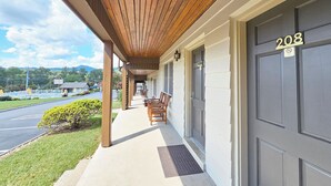 A covered porch with wooden beams, a row of chairs, and a door marked with the number 208. - The Parkman - Great Smoky Mountains (Townsend)