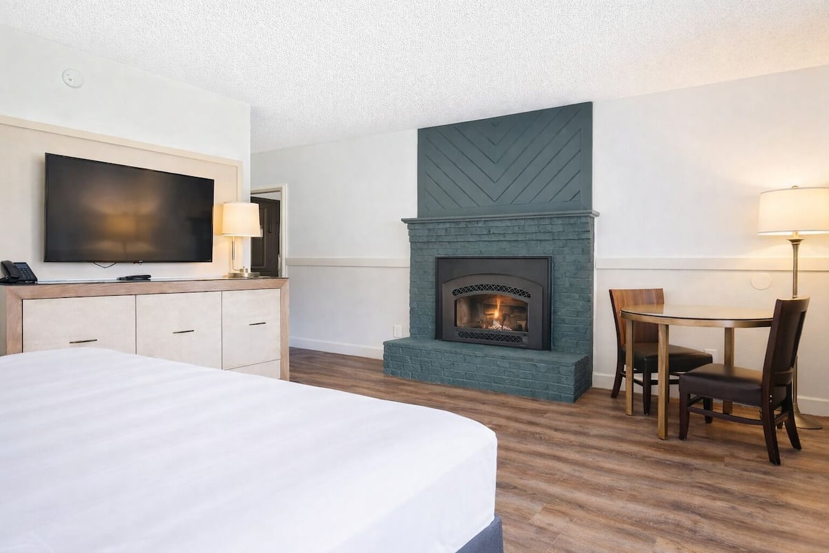 A hotel room with a bed, a television, a fireplace, a desk with a chair, and a lamp.