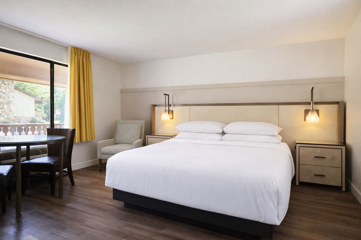 A bedroom with a bed, bedside tables, a chair, a table, and a window with curtains.
