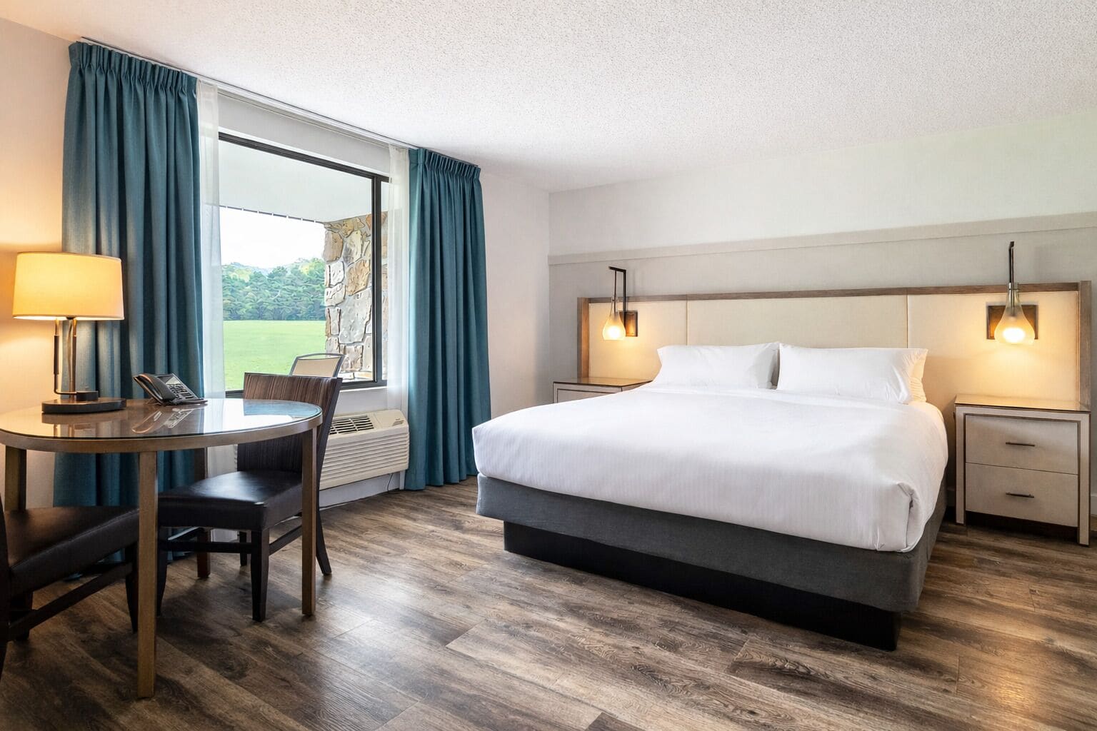 Hotelkamer met een bed, nachtkastjes, een bureau met stoel, een telefoon en een raam met gordijnen.