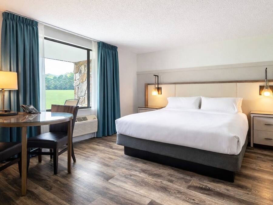 Hotelkamer met een bed, nachtkastjes, een bureau met stoel, een telefoon en een raam met gordijnen.