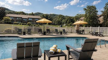A pool area with lounge chairs and umbrellas, surrounded by a fence and buildings in the background.