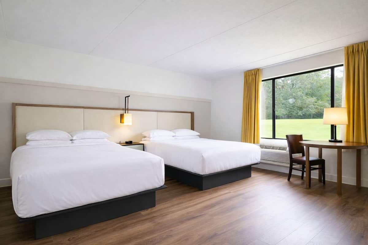 A hotel room with two beds, a desk, and a chair.