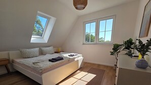Ein Schlafzimmer mit Bett, Nachttisch, Fenster, Pflanze und Schreibtisch.