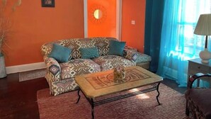 Ein Wohnzimmer mit einem gemusterten Sofa, einem Couchtisch und einem blauen Vorhang.
