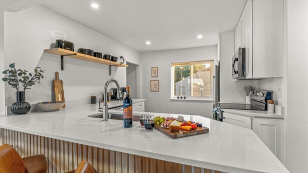A modern kitchen with a white countertop, wooden chairs, a wine bottle, and a fruit platter. - Mile High Retreat - Hot tub/Huge Backyard/Pool Table/Ping Pong/BoardGames/Arcade (Denver)