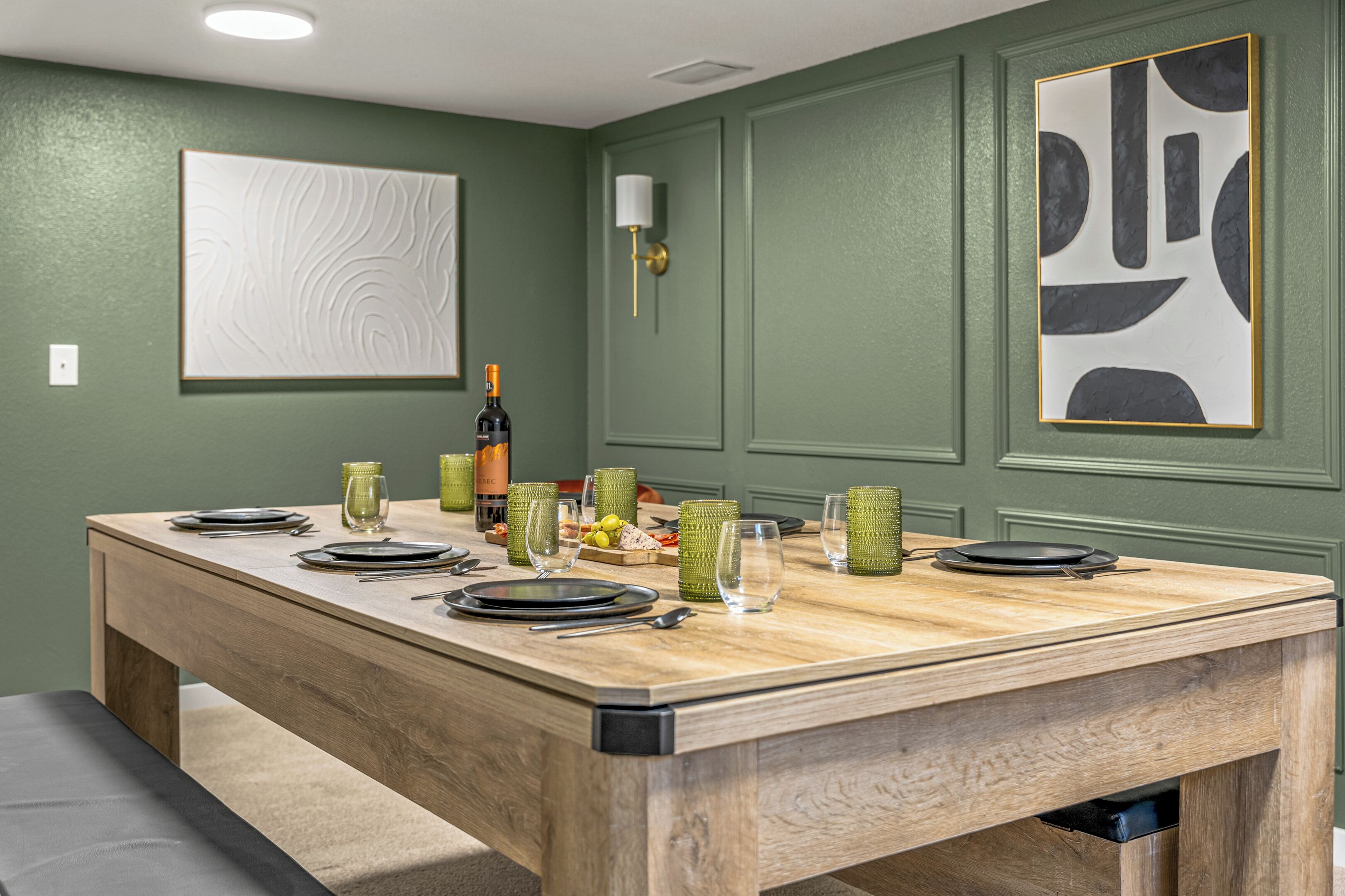 A dining area with a wooden table set for four, surrounded by green walls and modern art pieces.