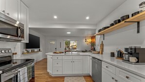 A modern kitchen with white cabinetry, a built-in oven, a microwave, and a coffee maker. - Mile High Retreat - Hot tub/Huge Backyard/Pool Table/Ping Pong/BoardGames/Arcade (Denver)