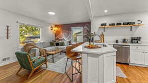 A modern kitchen with a central island, white cabinetry, and a dining area with a sofa and chairs. - Mile High Retreat - Hot tub/Huge Backyard/Pool Table/Ping Pong/BoardGames/Arcade (Denver)