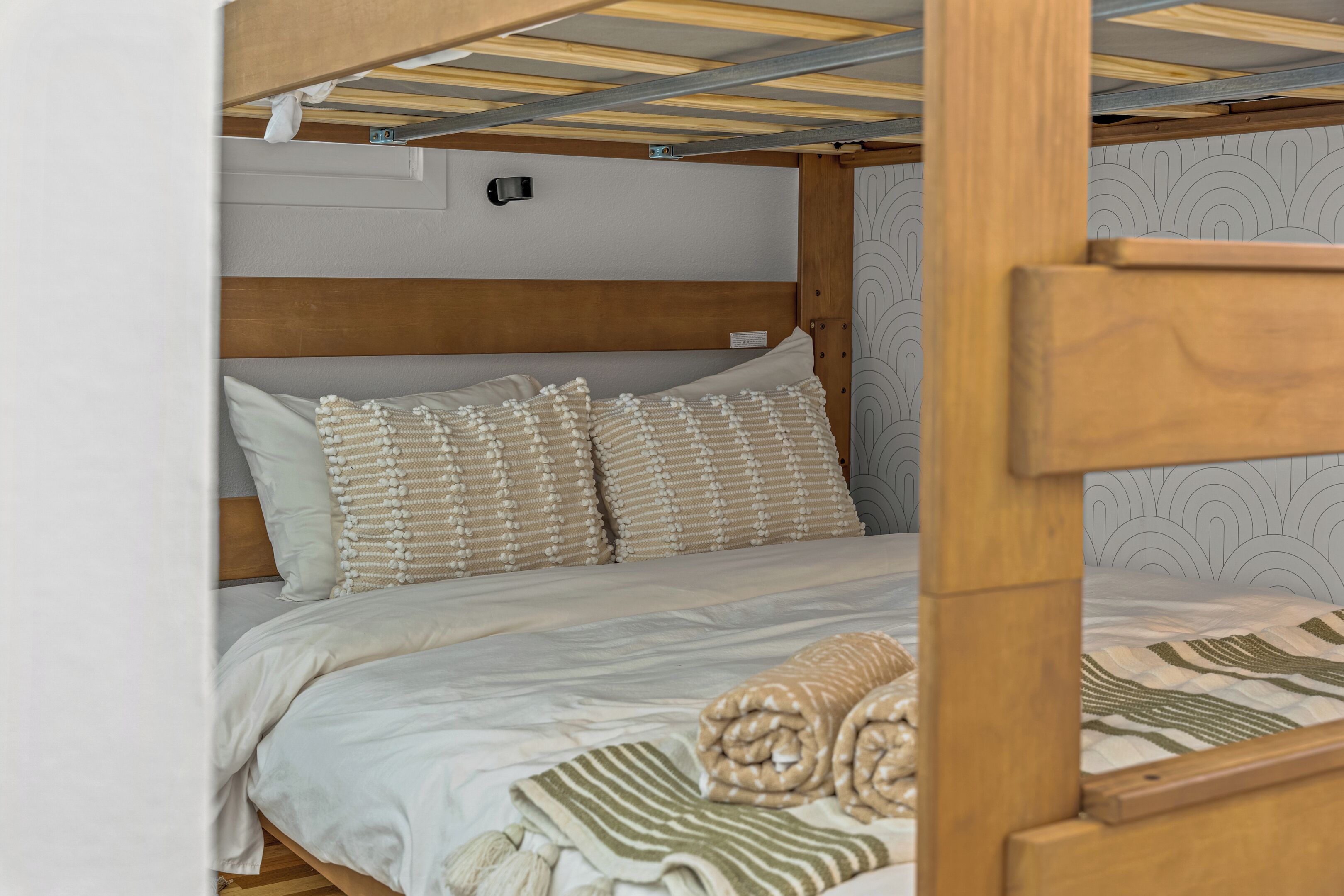 A bunk bed with a wooden headboard, white bedding, and patterned pillows.