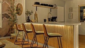 A modern kitchen with a wooden island, bar stools, a sink, and shelves with kitchenware. - Mile High Retreat - Hot tub/Huge Backyard/Pool Table/Ping Pong/BoardGames/Arcade (Denver)