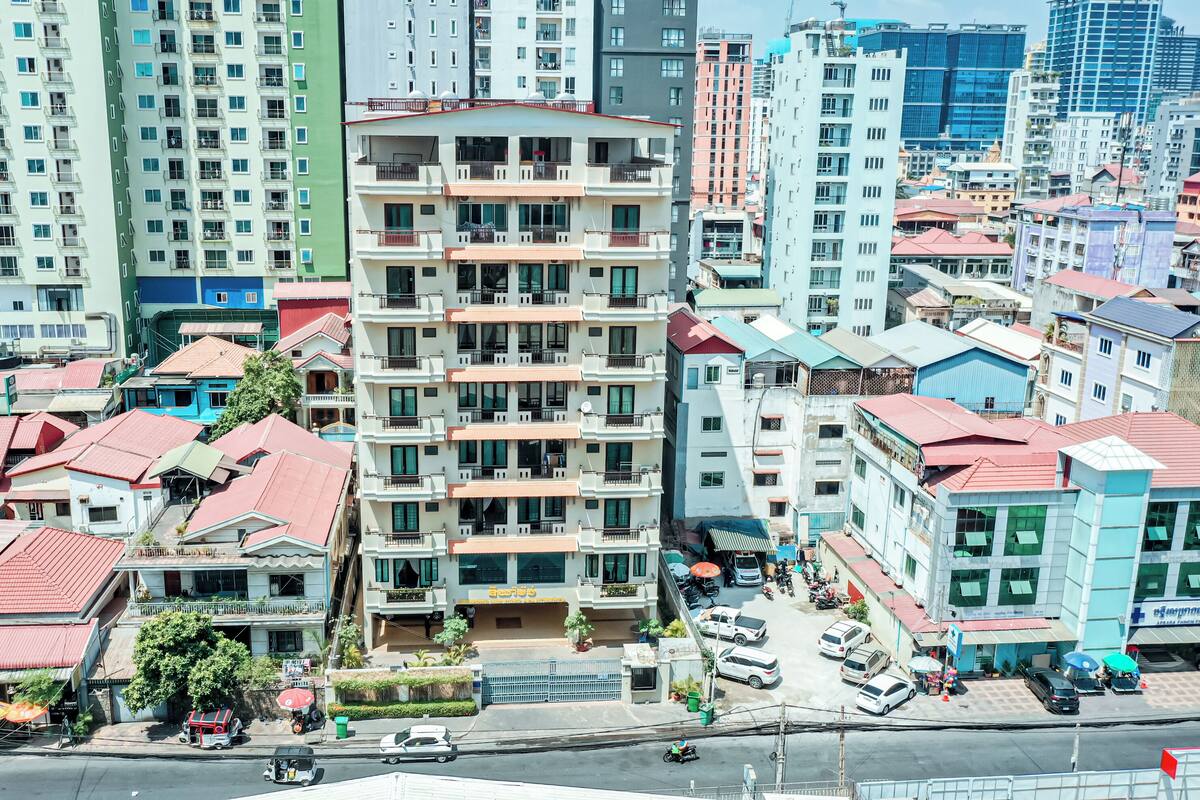 A multi-story building with balconies, a parking lot, and a street with vehicles.