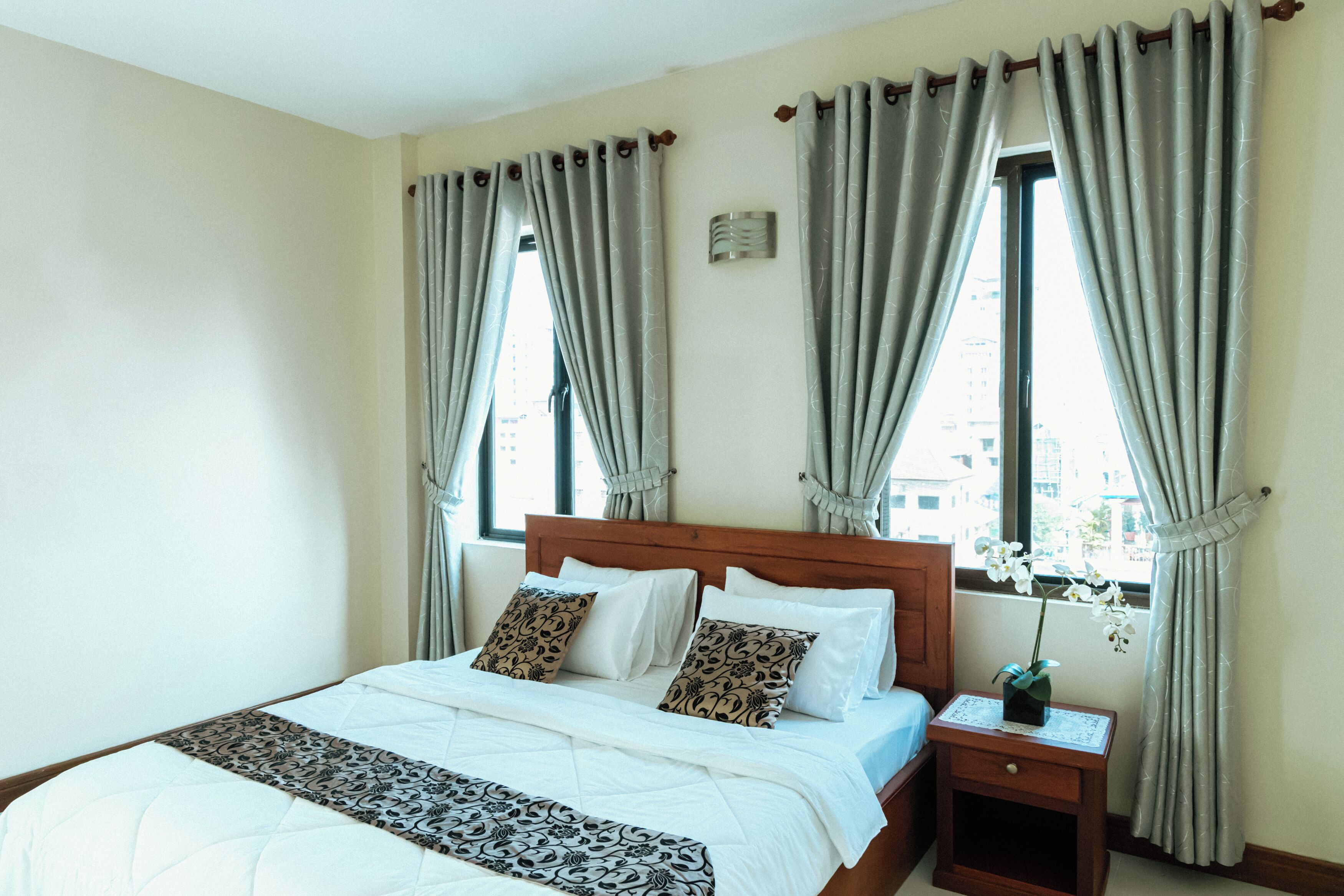 A hotel room with a bed, nightstand, and window with curtains.