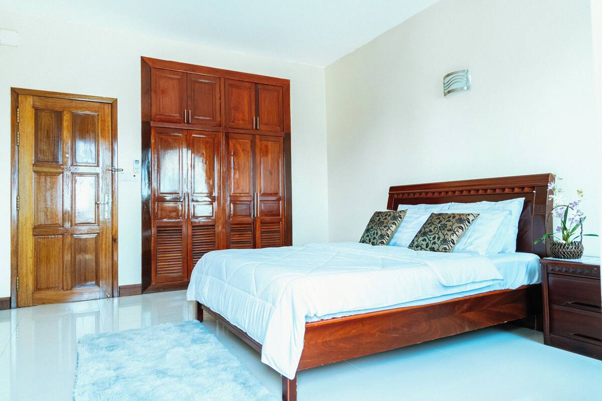A bedroom with a wooden bed, a large wardrobe, and a nightstand with a plant.