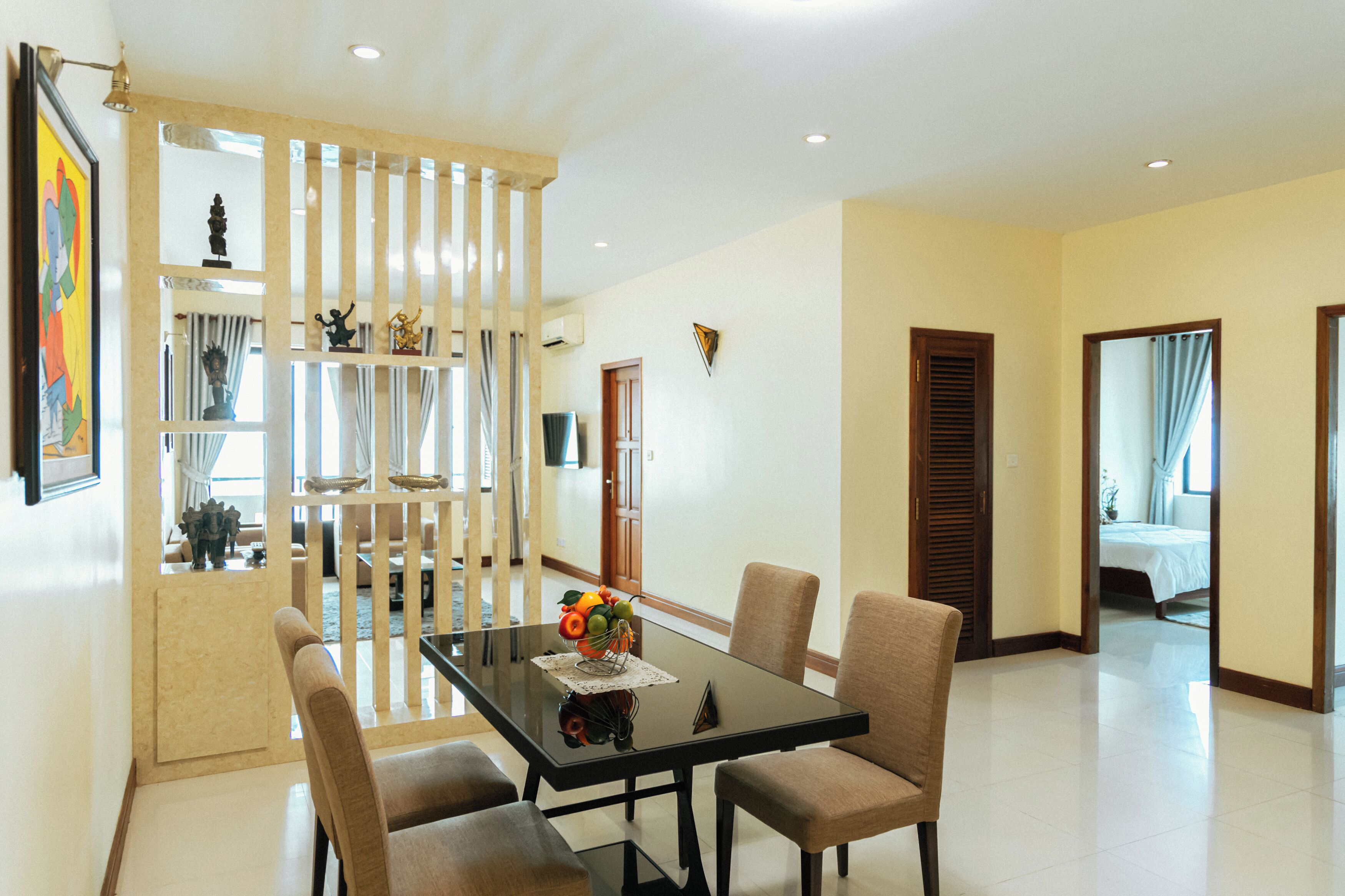 A dining area with a glass table, four chairs, and a fruit centerpiece.