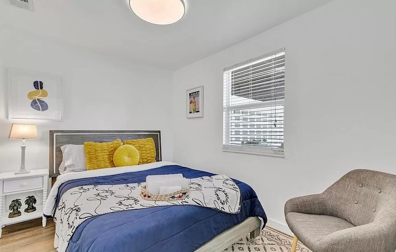 Une chambre à coucher avec un lit, une table de chevet, une chaise et une fenêtre avec des stores.