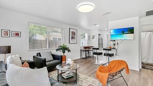 A modern living room with a sofa, coffee table, and TV. There is a dining area with a table and chairs.