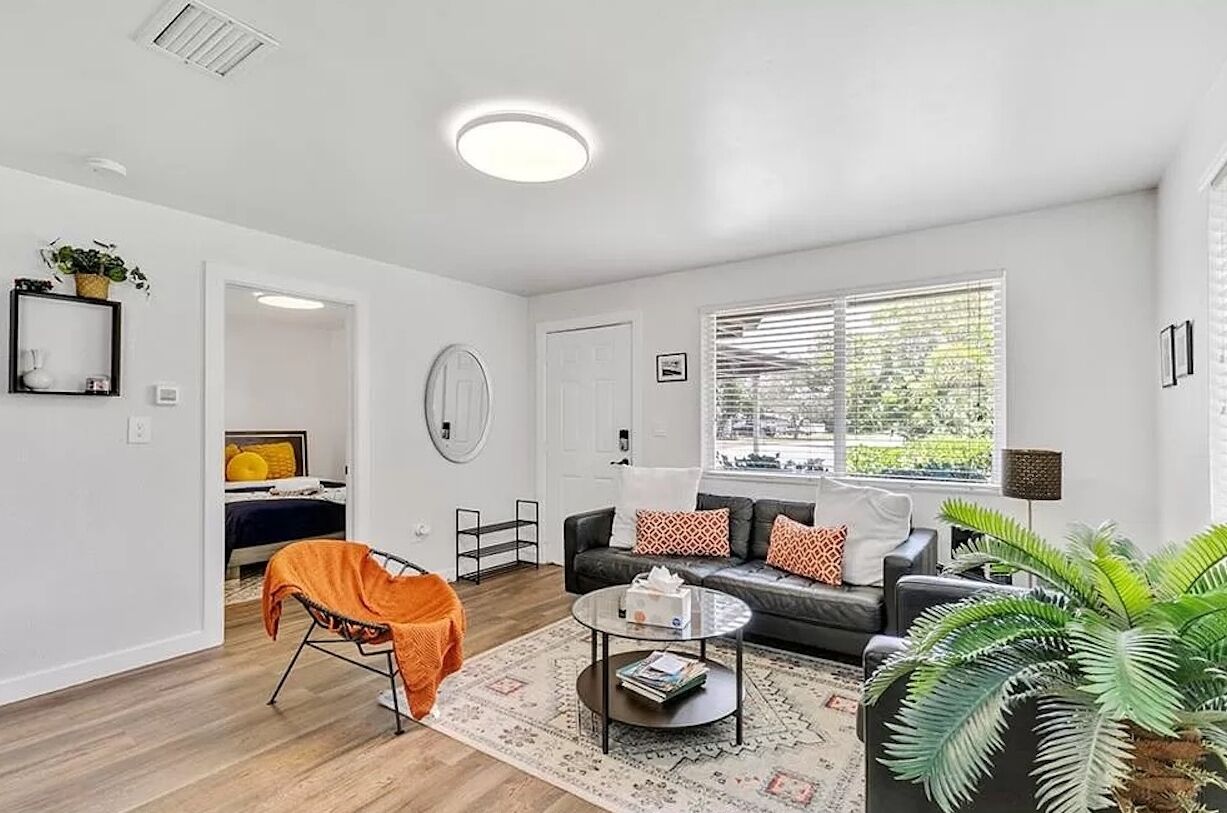 A modern living room with a sofa, coffee table, and a large window with blinds.