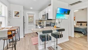 A modern kitchen with white cabinets, a microwave, and a large flat-screen TV mounted on the wall.