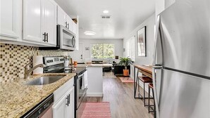 A modern kitchen with white cabinets, a granite countertop, stainless steel appliances, and a central island.