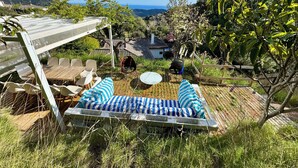 A patio with a wooden table and chairs, a swing, and a view of a house and hills in the background.