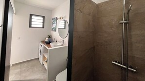 A modern bathroom with a shower, a sink, and a small window. - Le Ti Songe (Saint-Joseph)