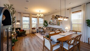 A spacious living room with a wooden dining table, comfortable seating, and a large window with curtains. - Cozy home near Med Center, NRG, UH, Downtown, Museum (Houston)