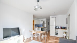 A modern living room with a flat-screen TV, a grey sofa, and a dining area with a white table and chairs.
