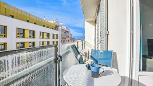 A balcony with a table and chairs, overlooking a coastal area with buildings.