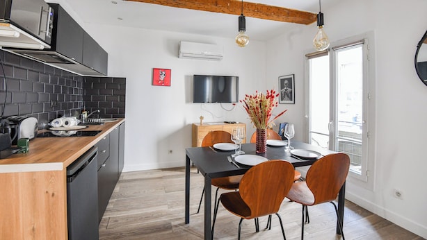 Una cocina moderna con isla de madera, armarios negros y una zona de comedor con mesa negra y sillas de madera.