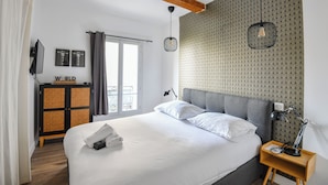 Un dormitorio con una cama grande, una mesita de noche de madera, un televisor montado en la pared y un papel tapiz estampado.