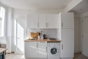 Eine kleine Küche mit weißen Schränken, einer Waschmaschine und einer Holz Arbeitsplatte.