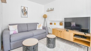Una sala moderna con un sofá gris, dos mesas redondas de madera, un televisor y un mueble de madera.