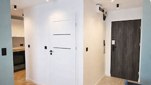 Un passadís amb una porta blanca, una porta de fusta fosca i una cuina amb armaris i forn.