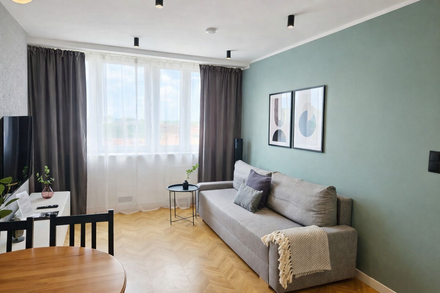 Un salon moderne avec un canapé, une petite table ronde et un fauteuil. Deux tableaux encadrés ornent le mur, et une plante est posée sur une table d’appoint.