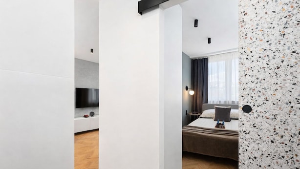 Habitació d'hotel moderna amb televisió de pantalla plana, un llit amb capçaleri fosca, una taula de nit amb una làmpada i vista a la ciutat per la finestra.