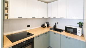 Cuina moderna amb armaris blancs, fogó d'inducció negre, forn de microones integrat i un rentaplat amb aixeta negra.