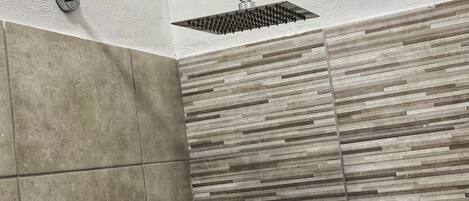 A shower with a handheld showerhead and a textured wall.
