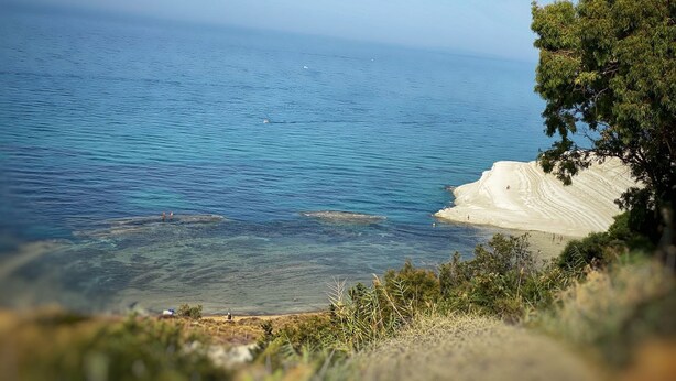 A coastal landscape with clear blue sea, sandy beach, and greenery. - TerrazzaRooms (Realmonte)