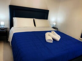 Una cama bien hecha con un edredón azul, almohadas blancas y dos toallas dobladas sobre la cama.