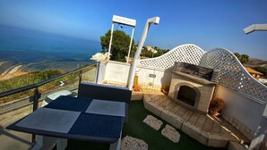 A terrace with a view of the sea, a seating area with a table, and a stone fireplace. - TerrazzaRooms (Realmonte)
