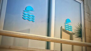 A building facade with large windows featuring a stylized wave logo. - TerrazzaRooms (Realmonte)