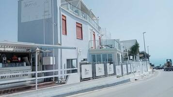 A coastal building with a restaurant on the ground floor, a white facade, and red shutters.