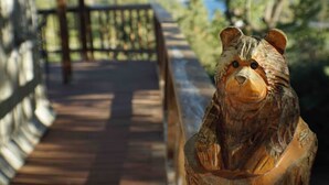 Un banco de madera con una figura de oso tallada, un muelle de madera y vistas a árboles y colinas al fondo.