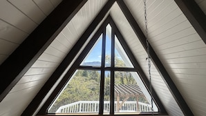 Una ventana de techo triangular con vistas a una terraza de madera y árboles.