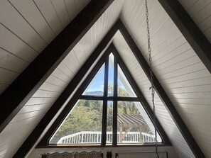 A triangular attic window with a view of a wooden deck and trees.