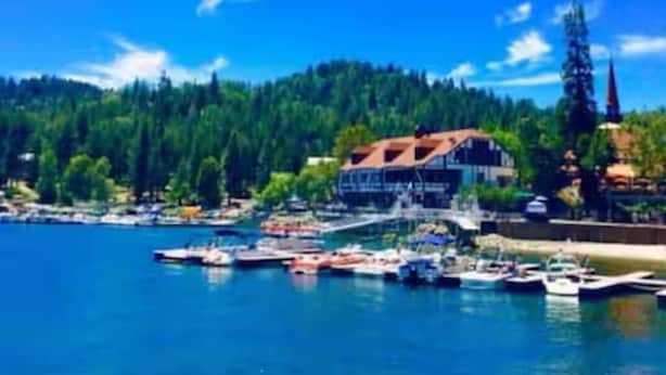 Un pueblo costero con un puerto deportivo, barcos y un edificio destacado de techo rojo.